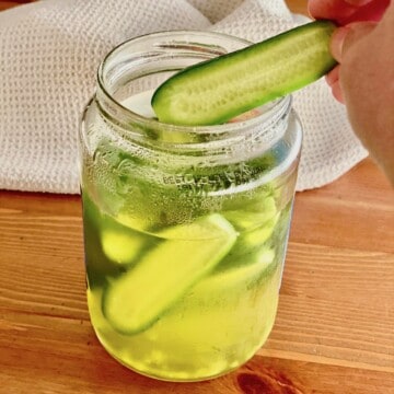 a jar of pickles with one being removed to eat.