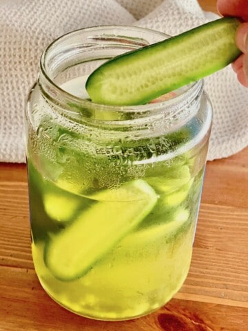 a jar of pickles with one being removed to eat.