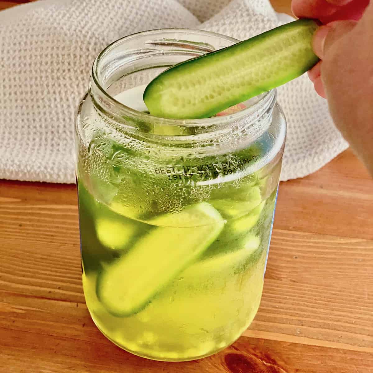 a jar of pickles with one being removed to eat.