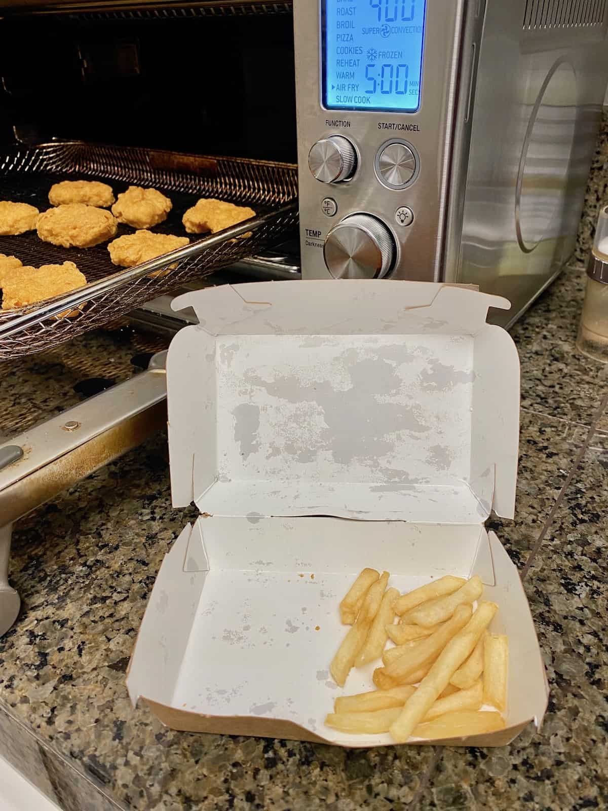 Open box with fries in it and nuggets on air fryer tray.