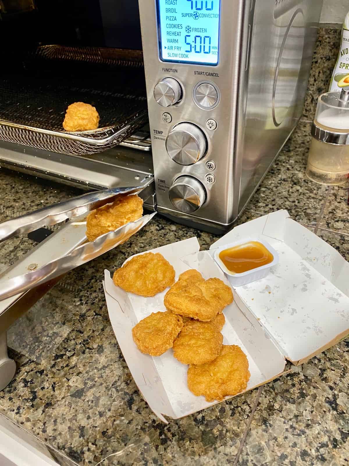 Using tongs to remove hot McNuggets from air fryer.