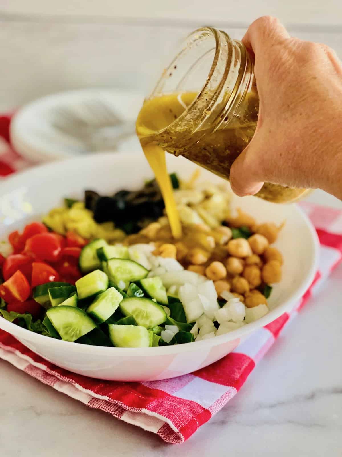 Hand pouring vegan italian dressing from a jar onto the bowl of salad.