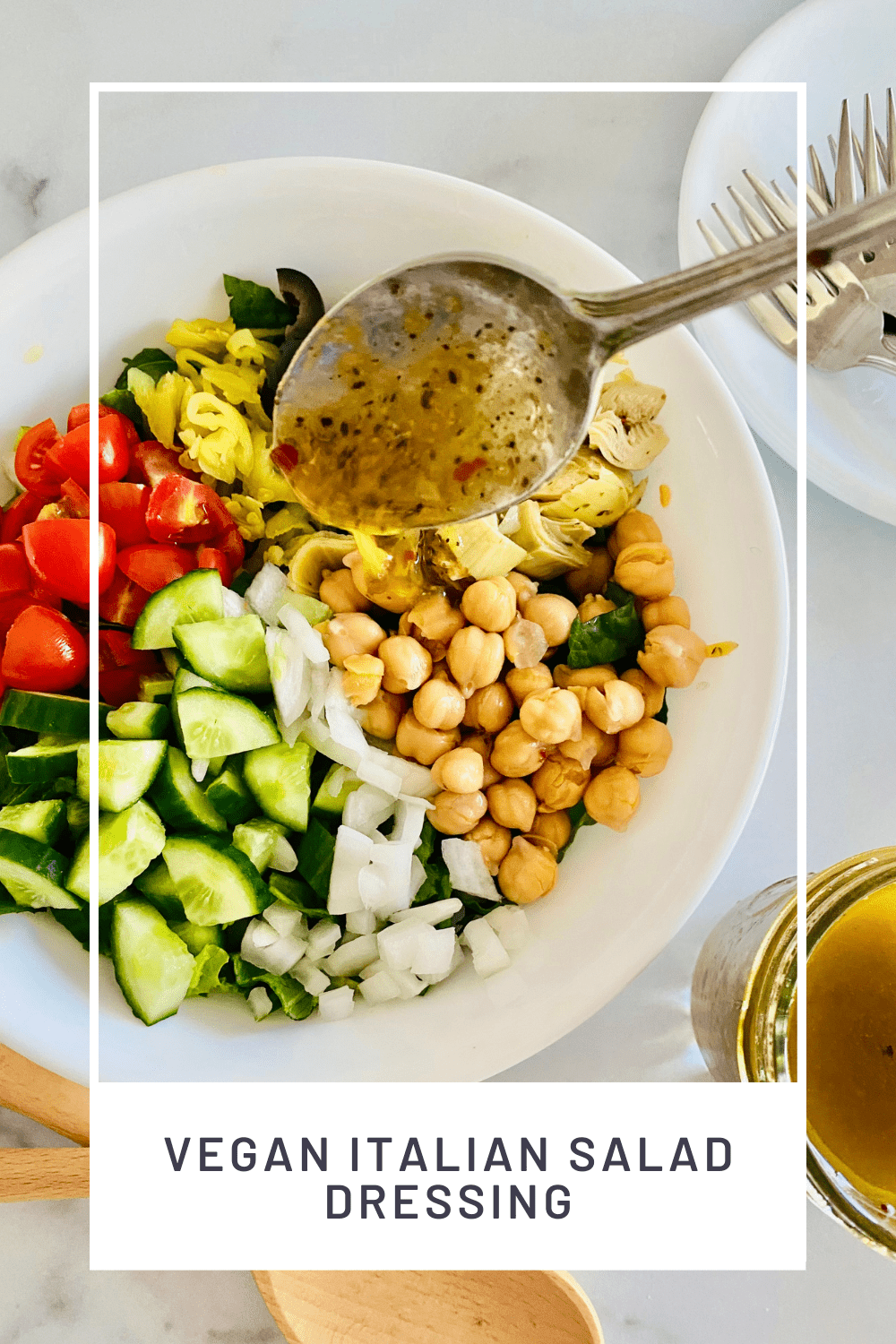 Spoon drizzling dressing over a salad with cucumbers, tomatoes, garbanzo beans, and more. 