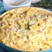 A teal casserole dish with bubbling penne pasta with ham.