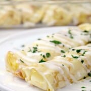 Two plates crepes ready to eat and covered in white bechamel sauce.
