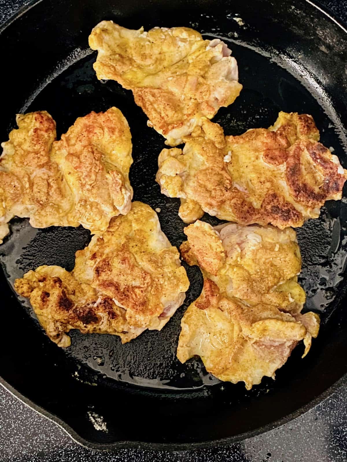 Chicken Thighs golden brown and cooked in a cast iron pan.