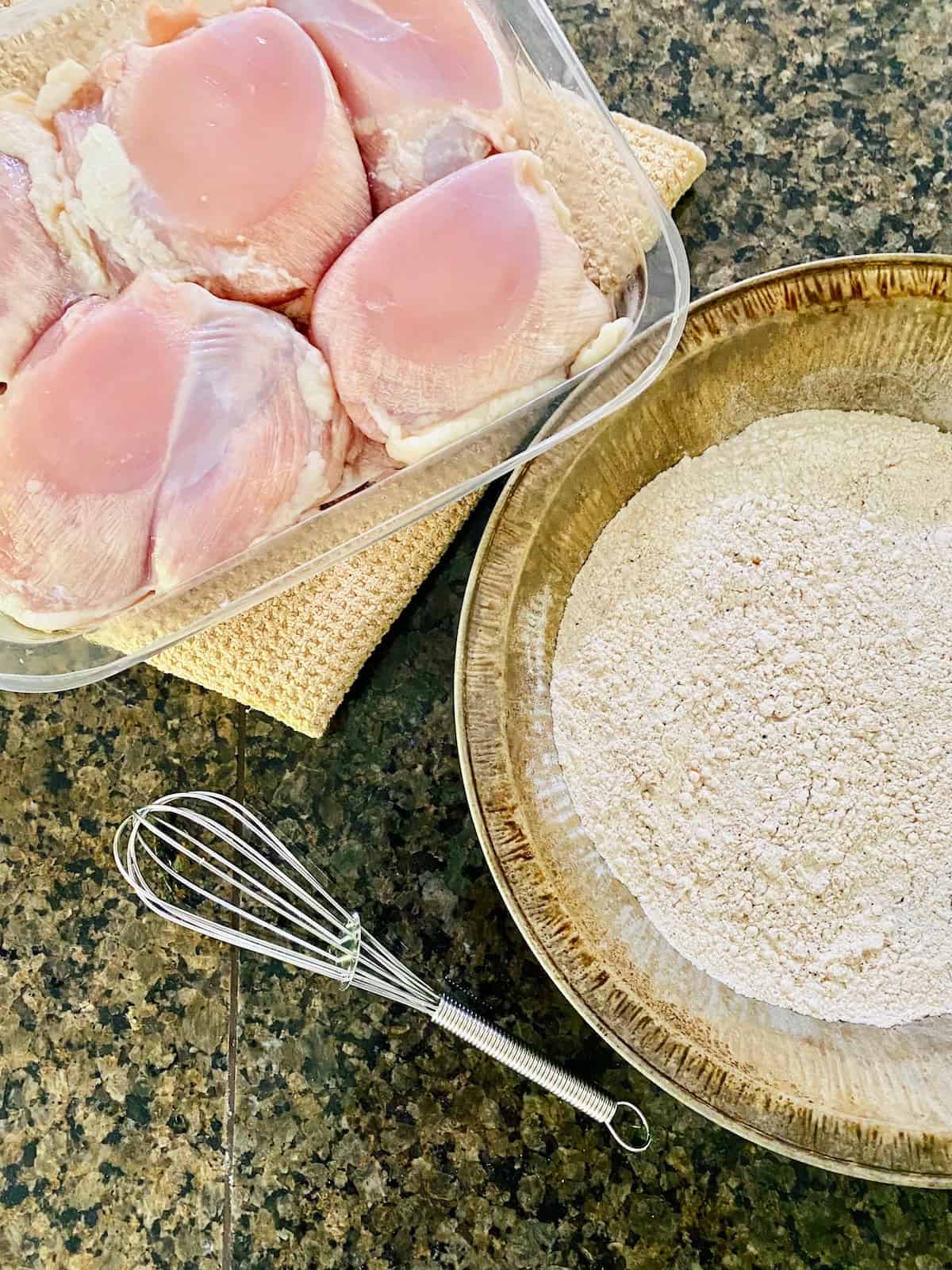 Thighs next to seasoned flour in a dish.