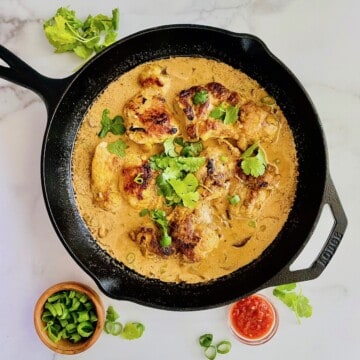 Creamy Coconut Chicken in a cast iron skillet garnished with chili garlic sauce and cilantro.