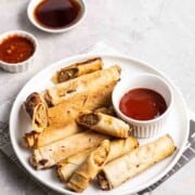 Vegan lumpia that has been air fried is on a platter with a dipping sauce.