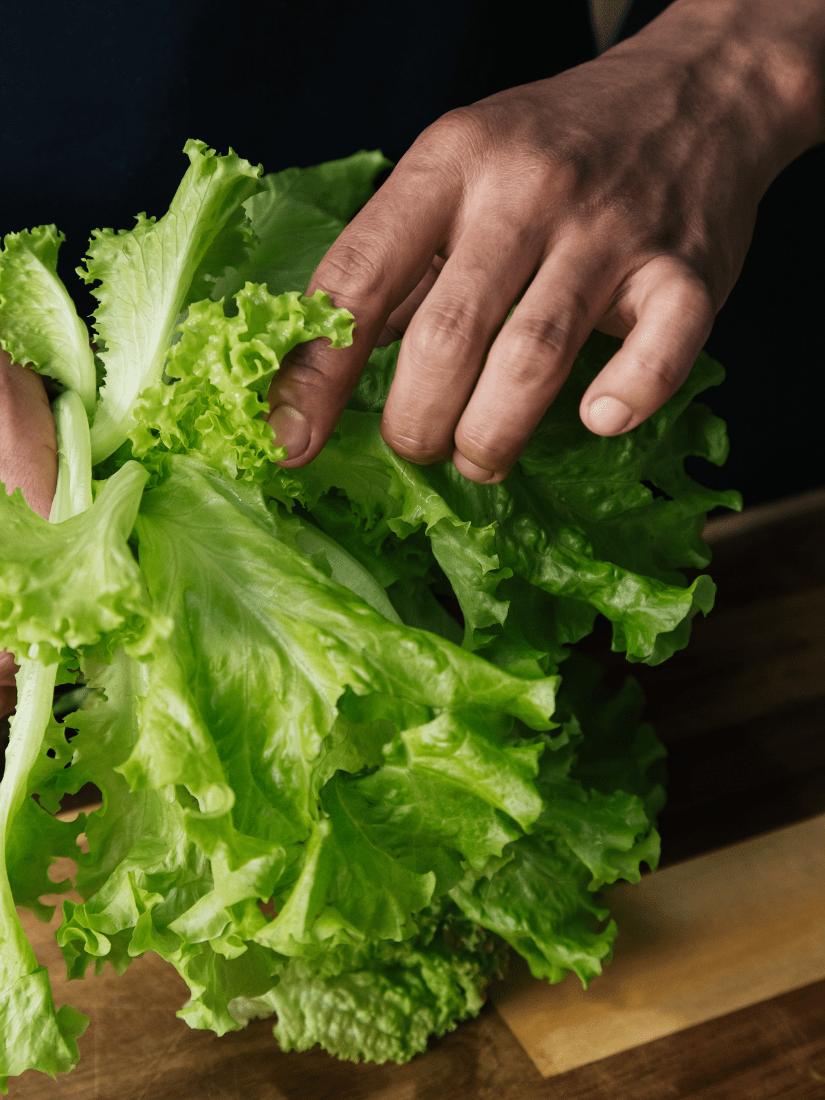 Hand holding lettuce to chop on a cutting board.