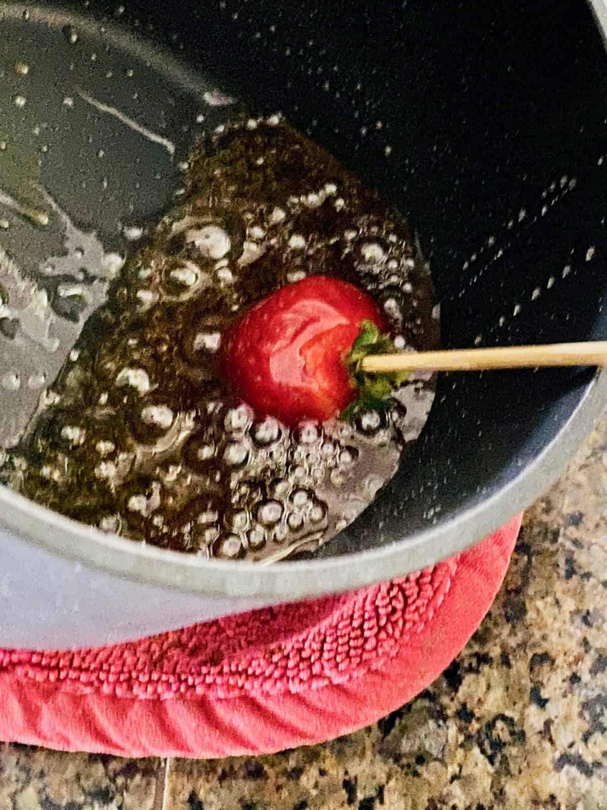 Rolling a skewered strawberry in hot melted sugar for candied Tanghulu.