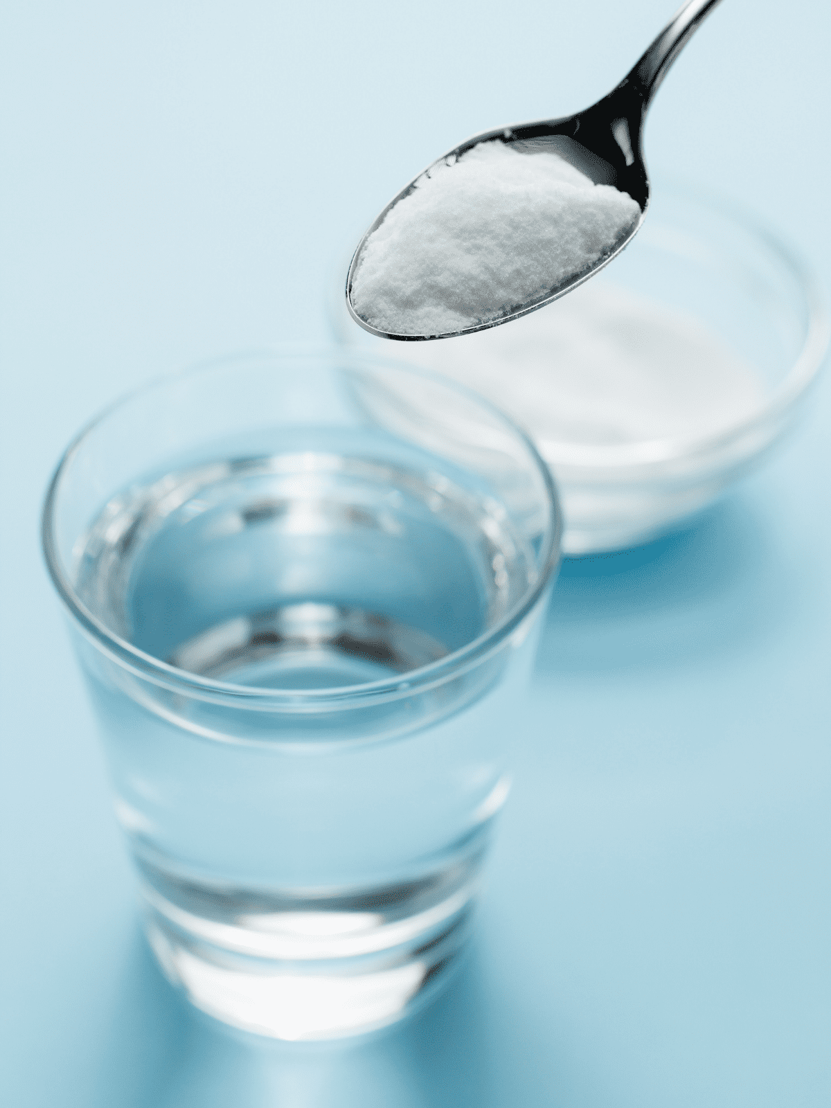 A glass of water next to a small bowl of baking powder or soda. 