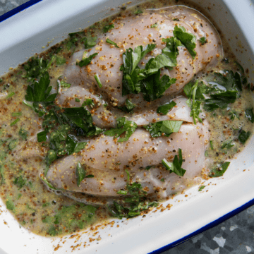 Chicken marinating in a white dish.