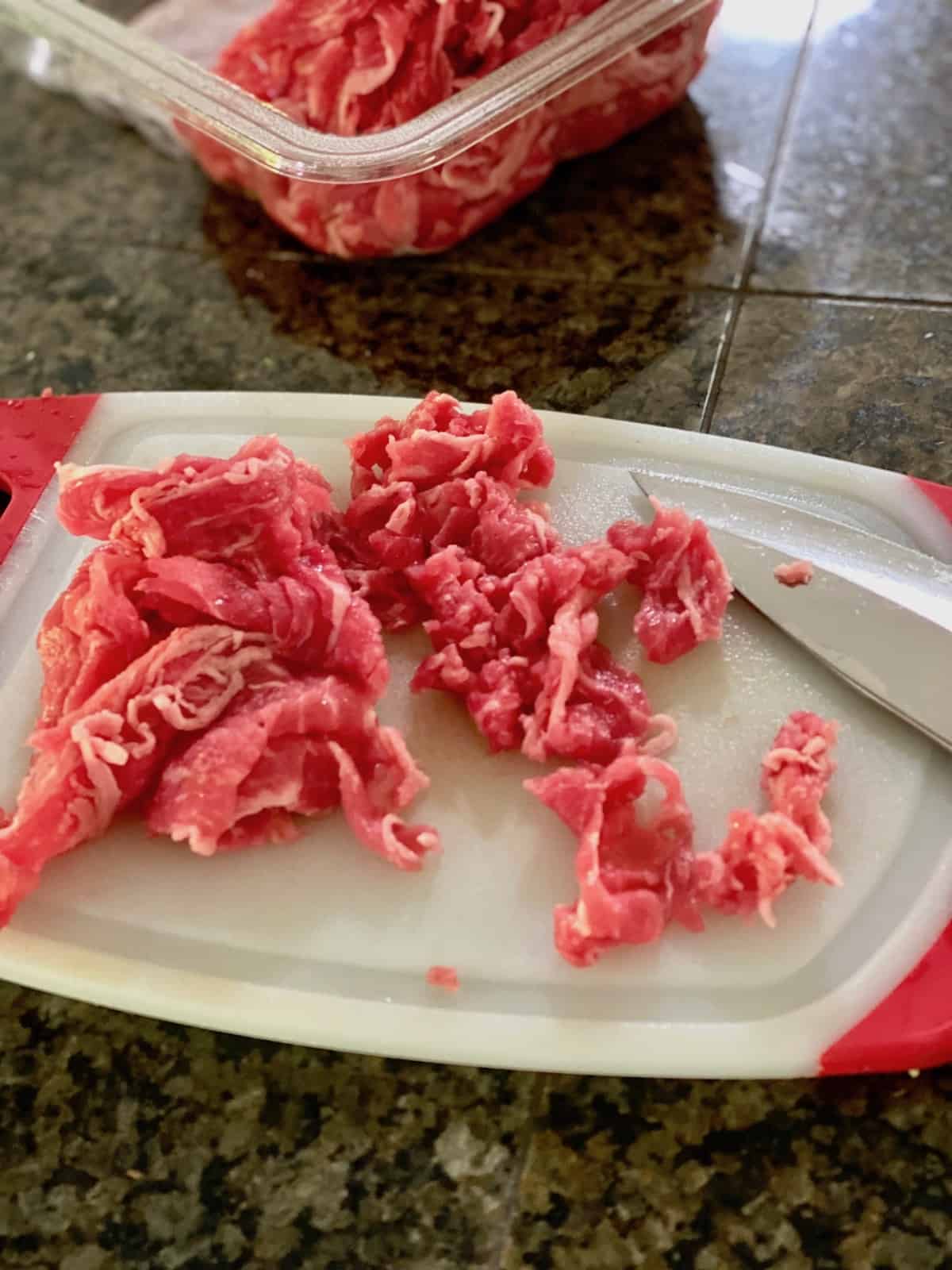 Cutting the shaved beef into smaller pieces on a cutting board.