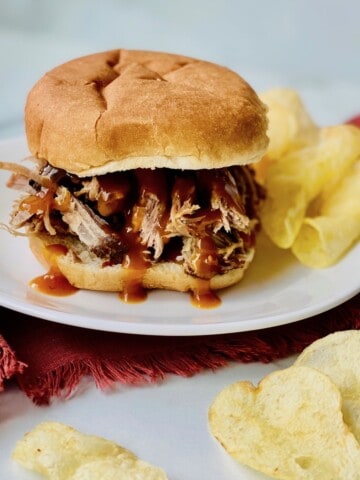 Smoked Pulled Pork Shoulder (pork butt) Featured Pulled Pork with BBQ sauce on a bun plated with chips