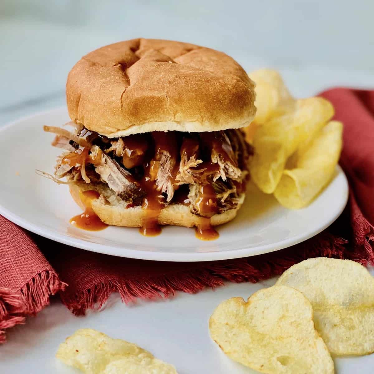 Smoked Pulled Pork Shoulder (pork butt) Featured Pulled Pork with BBQ sauce on a bun plated with chips