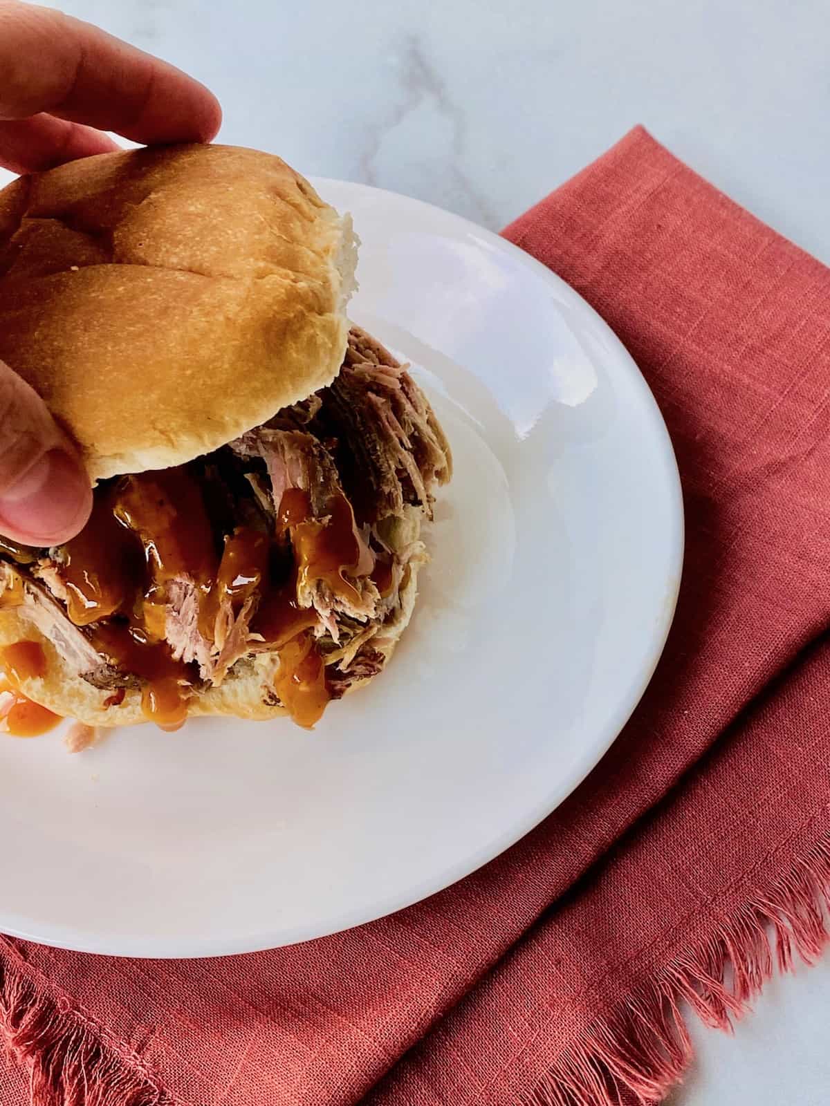 Smoked Pulled Pork Shoulder (pork butt) Hand adding the top bun to a pulled pork with bbq sauce sandwich.