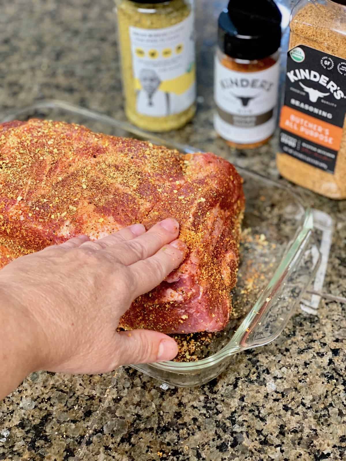 Hand pressing the seasonings all over the flesh of the pork butt before smoking.