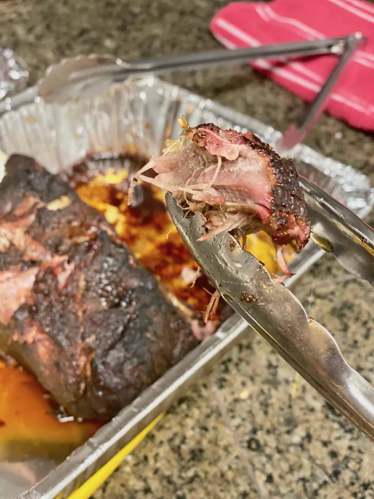 Tongs holding a cooked piece with juicy inside and seasoned dark crust outside of the pork roast.