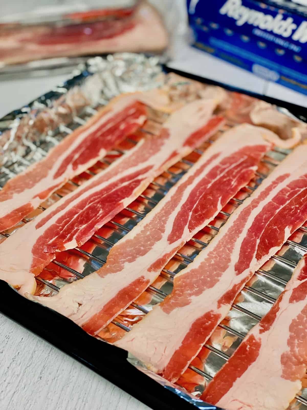 Raw bacon lined up on a baking rack lined with foil over the bottom pan.
