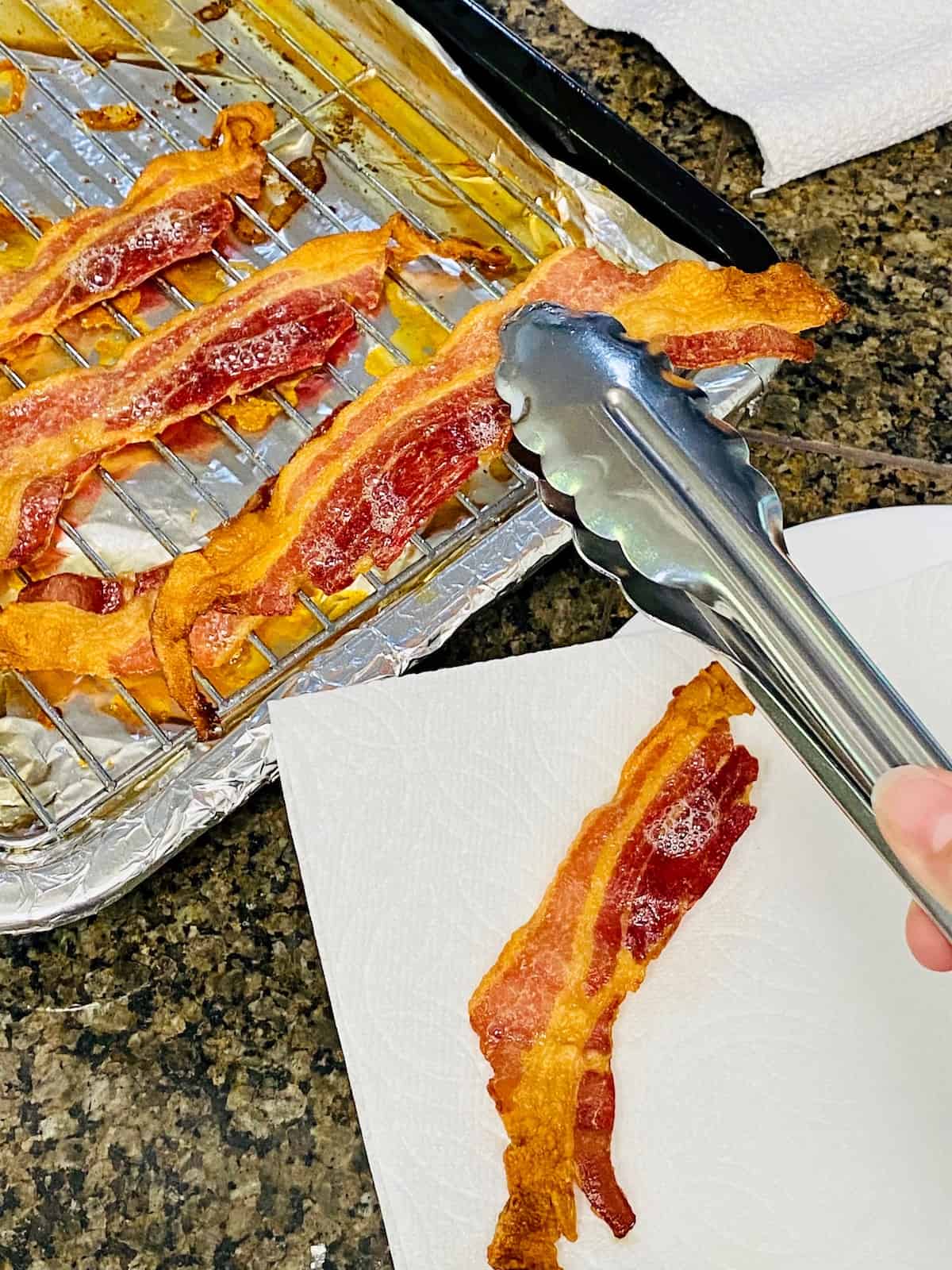 Tongs placing bacon on paper towels.