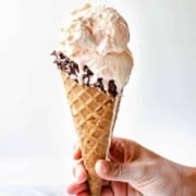 A cone dripping with a scoop of white chocolate peppermint ice cream.
