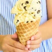 A child holding a cone with a scoop of chocolate chip ice cream.