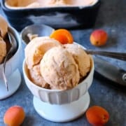 A bowl of apricot mascarpone ice cream on a table with fresh apricots around it.