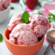 A red bowl with 3 scoops of strawberry mint ice cream.