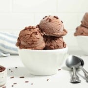 Vegan chocolate ice cream in a bowl with a spoon on a table.