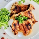 A plate with 3 grilled boneless chicken thighs will grill marks and parsley on top.