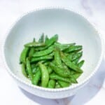 A white bowl with snap peas seasoned and air fried.