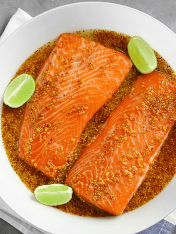 Salmon filets in a dish with marinade and limes.