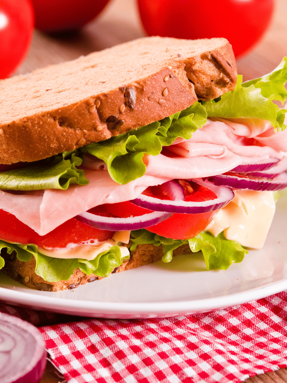 White plate with a sandwich packed with cold cuts and produce. 