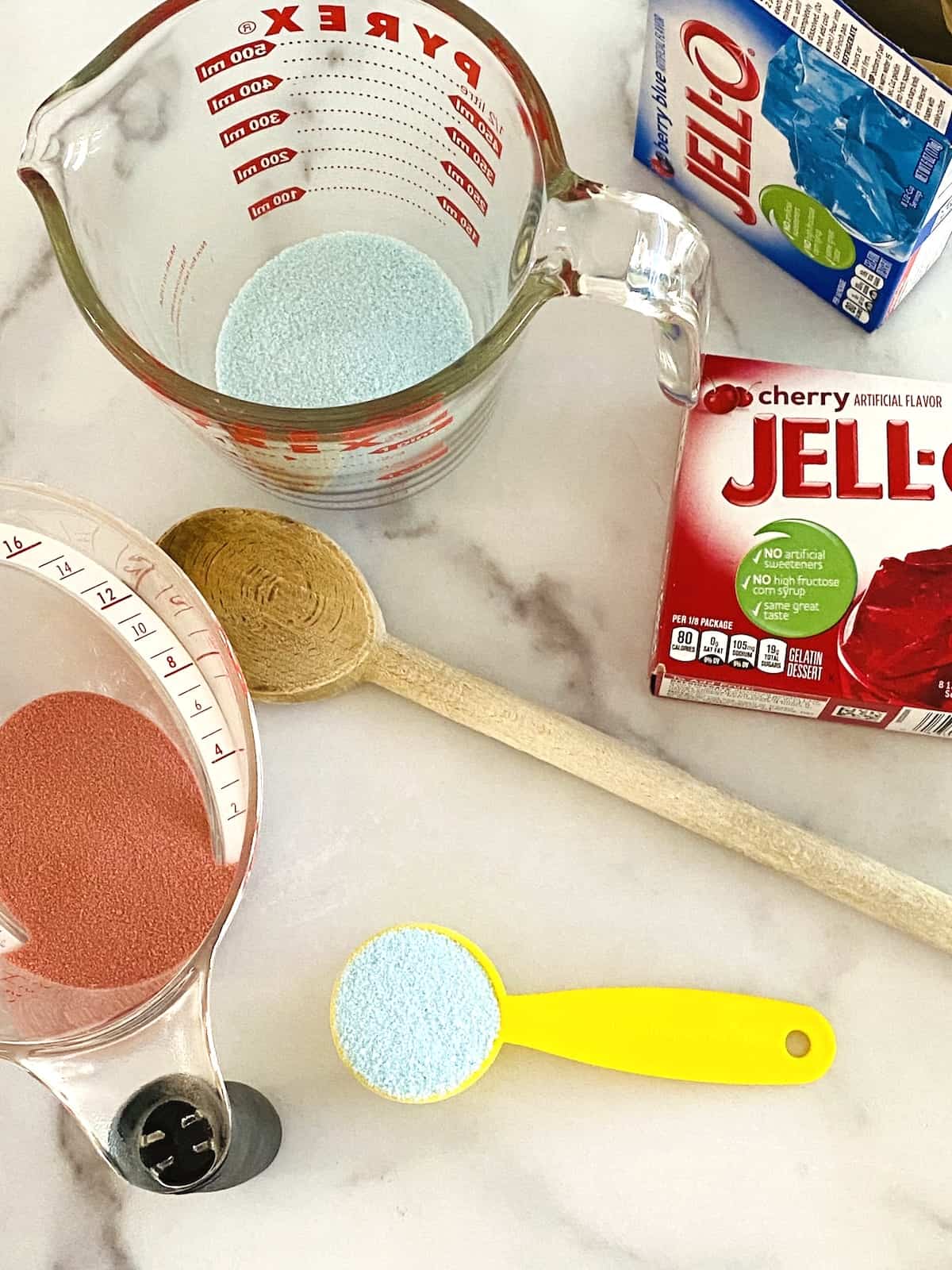 Measuring glasses overhead with gelatin powder plus open Jello Boxes on the counter for poke cake.