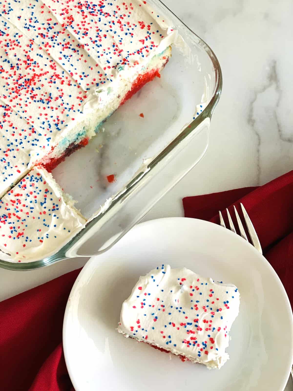 Patriotic Red, White, & Blue Poke Cake Overhead of cut cake and slice on a plate.