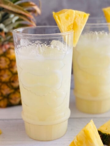 Two glasses filled with pina colada on the rocks and garnished with fresh pineapple wedges.