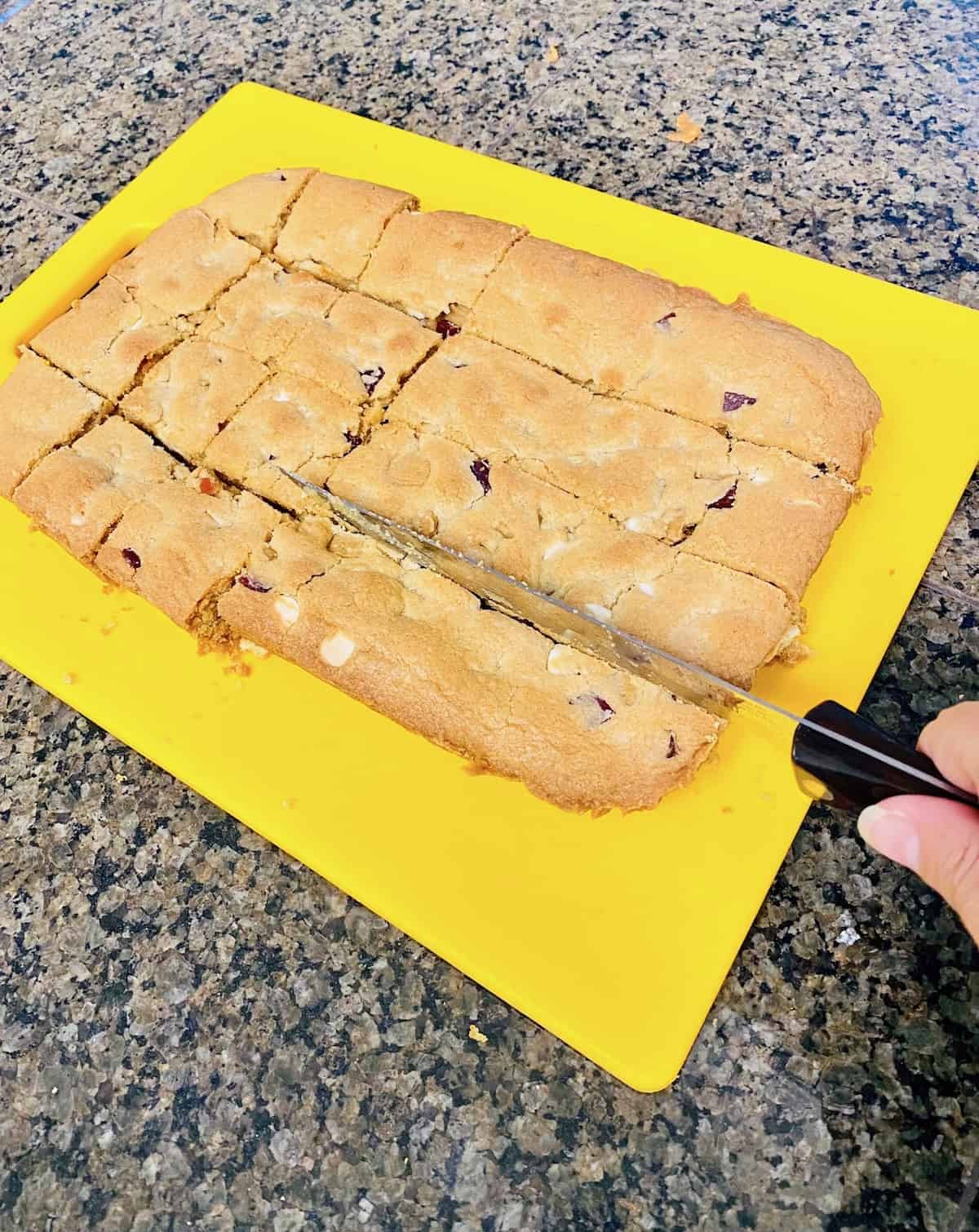 Cutting board with the batch of cookies on it as knife cuts through the slab into cookie square.