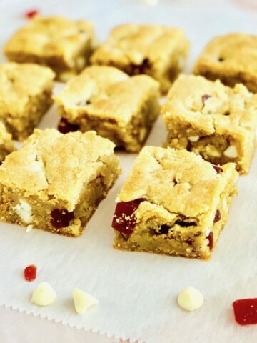 Strawberries and cream cut cookie bars on white parchment showing white chocolate chips and strawberry pieces.