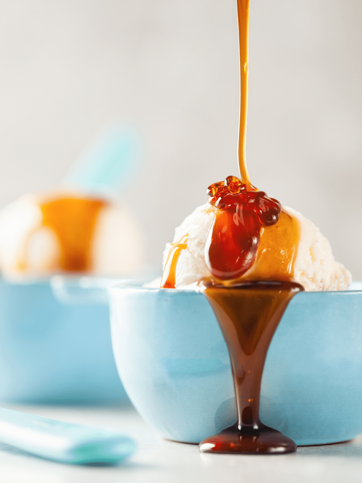 Blue bowls filled with vanilla ice cream and caramel sauce pouring down and over it.