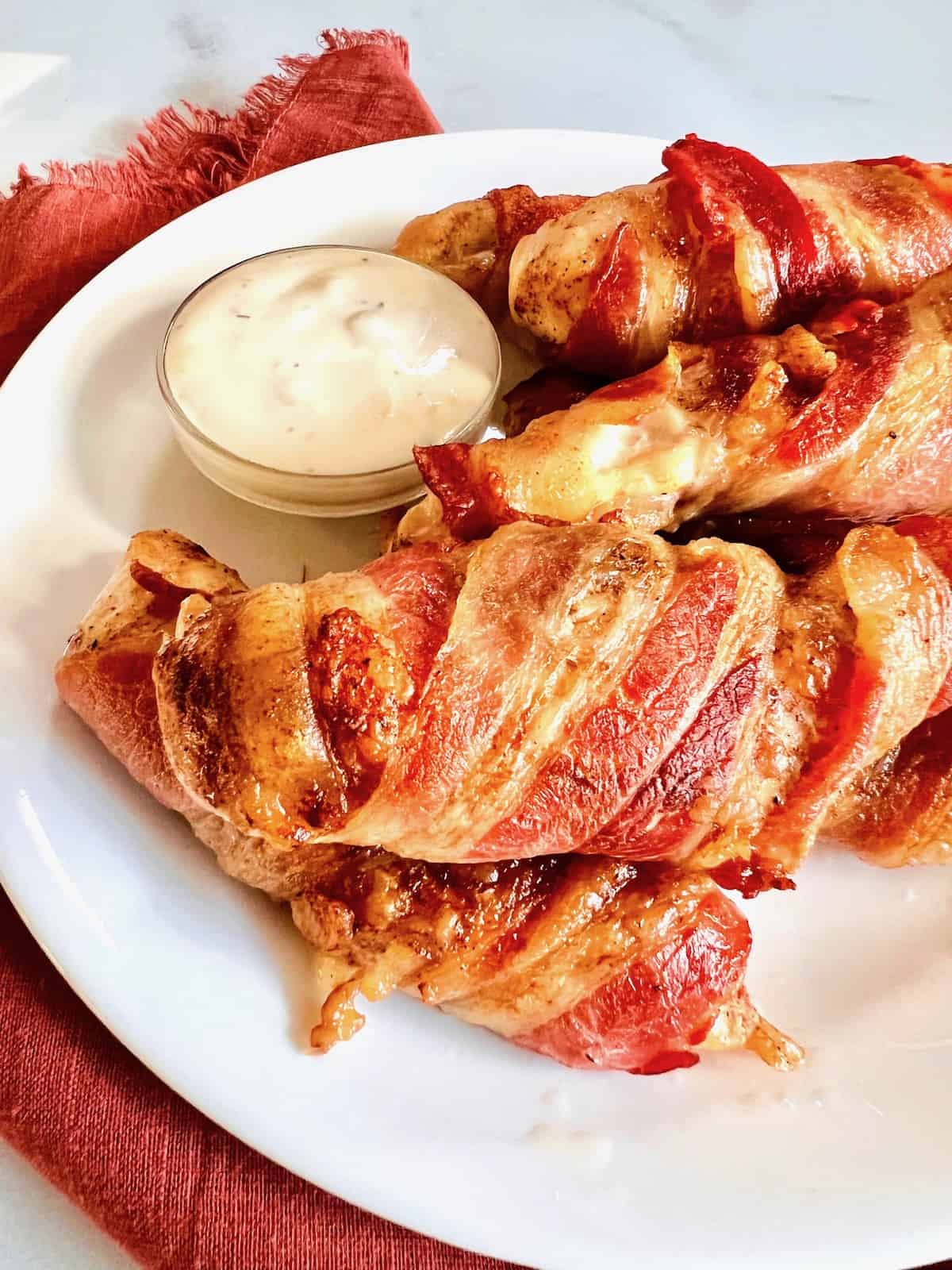 A stack of bacon-wrapped chicken tenders lated with blue cheese dip.