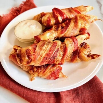 Plated chicken tenders wrapped in crispy bacon and blue cheese dip on the side.