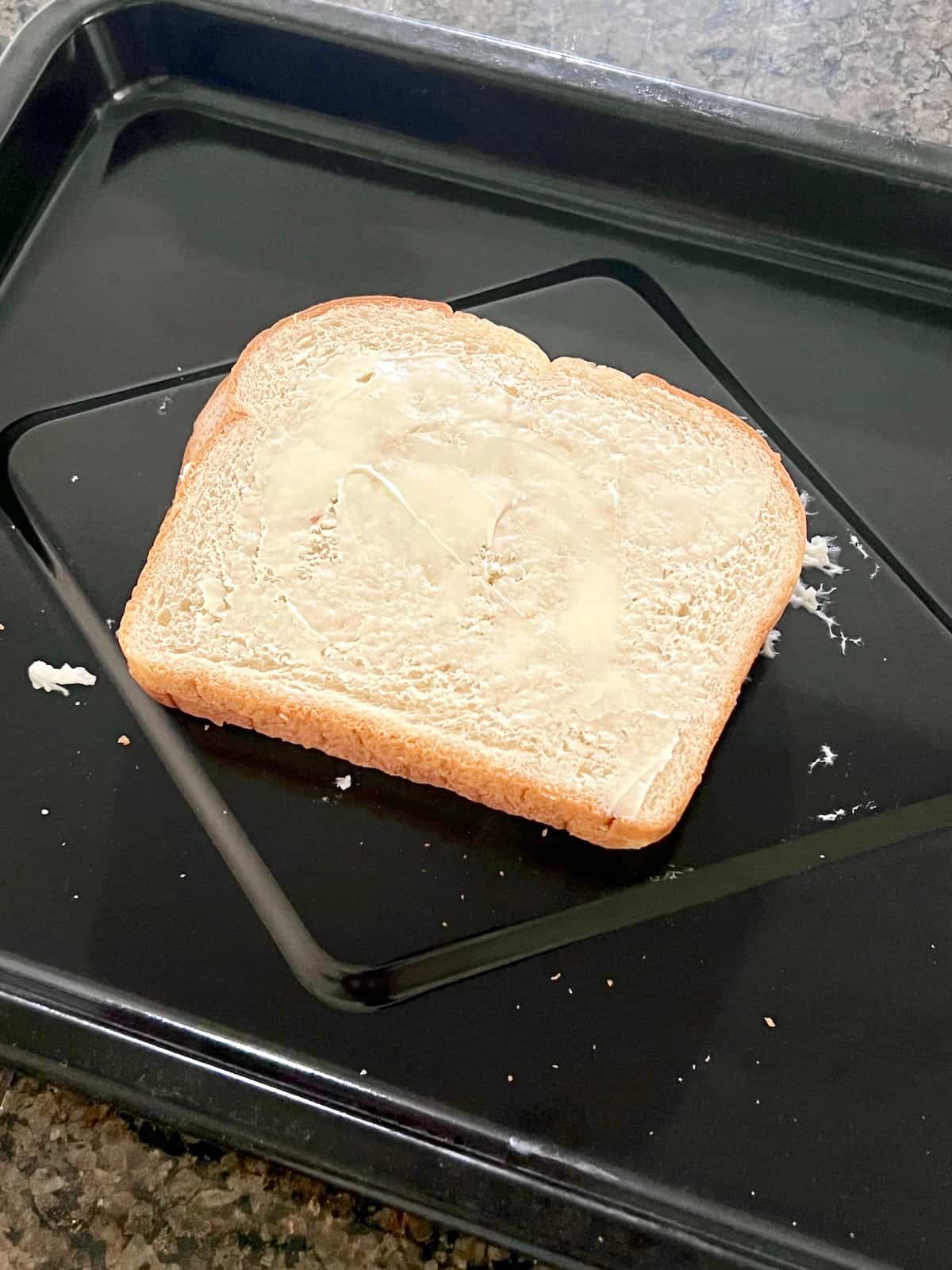 Baking tray with a prepared sandwich with butter facing up on the bread.