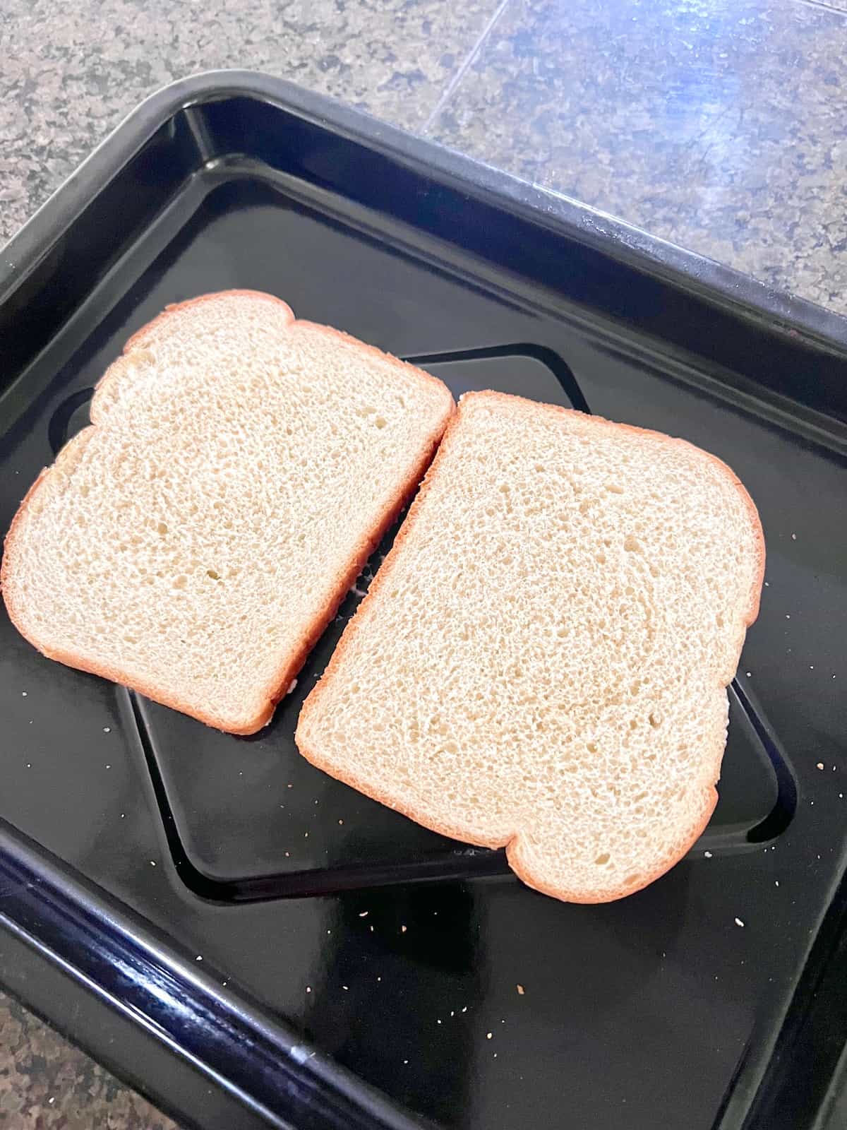 Two buttered slices on a baking tray ready to be topped with sliced cheddar.