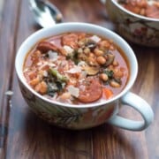 Sausage and white bean kale stew in a white mug ready to eat.