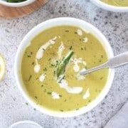 Bowl of creamy asparagus soup with a spoon and topped with cream.