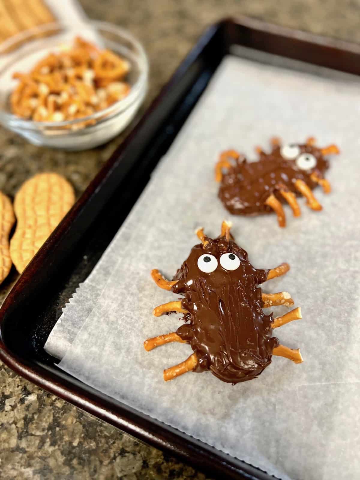 Two chocolate dipped cookies decroate to look like spiders sitting on parchment.