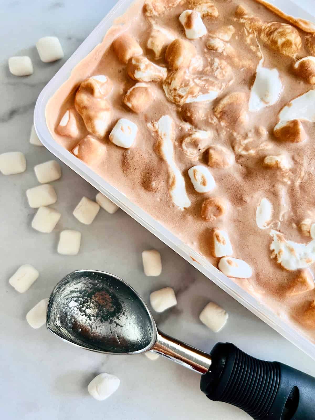 Chocolate Marshmallow Ice Cream Frozen in the container with an ice cream scoop and marshmallows on the counter.