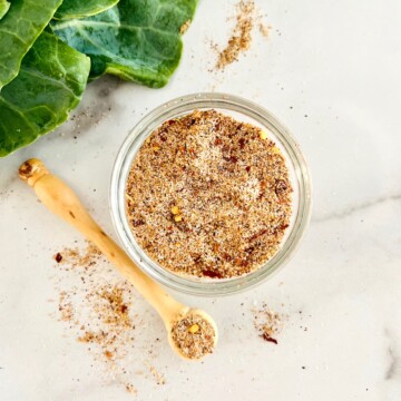 Seasoning blend in a bowl with collard greens on a table.