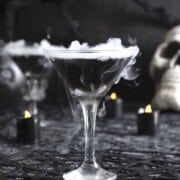 A martini glass filled with black vodka and dry ice smoking on the top.